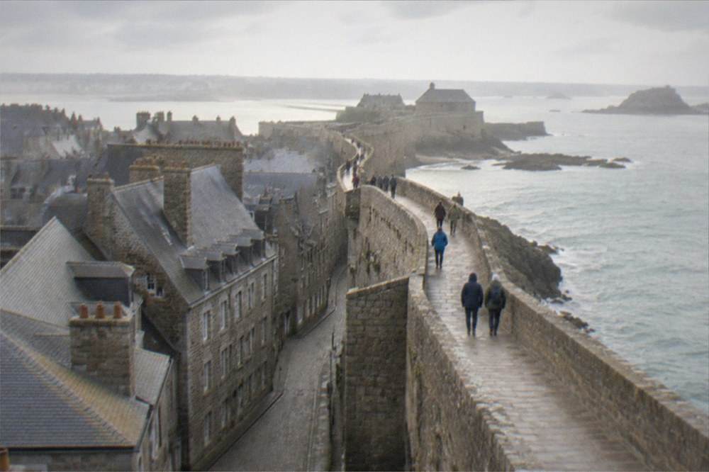 Visitors in windproof jackets walking a sea wall under a partly cloudy sky