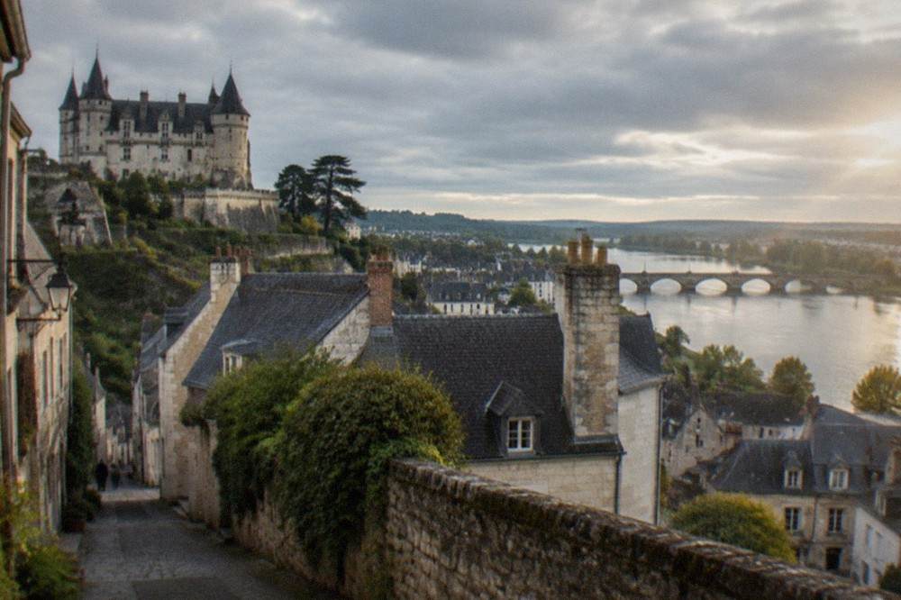 A narrow street of old stone houses with slate roofs leading down toward a river, morning light on the walls