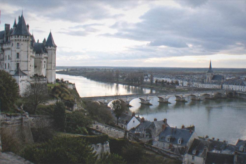 A long stone bridge crossing a wide river toward a town with a church spire, calm water reflecting the evening sky
