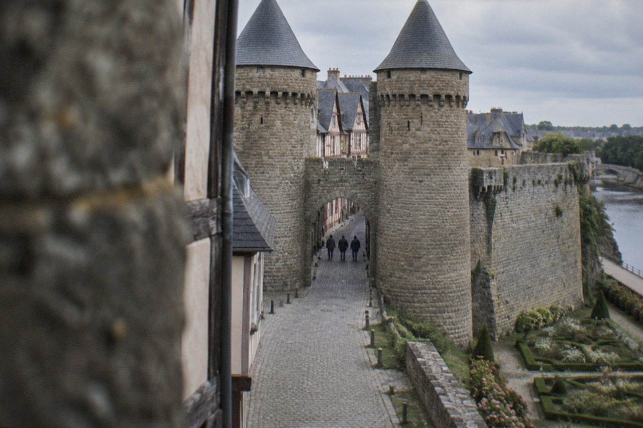 Medieval stone gateway with twin towers opening onto a cobbled street of half-timbered houses in a walled Breton town