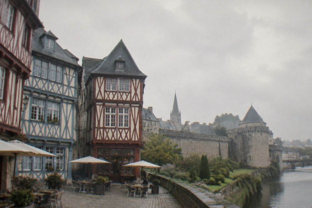 Half-timbered houses with painted wooden beams on a square in a medieval Breton town, café tables below