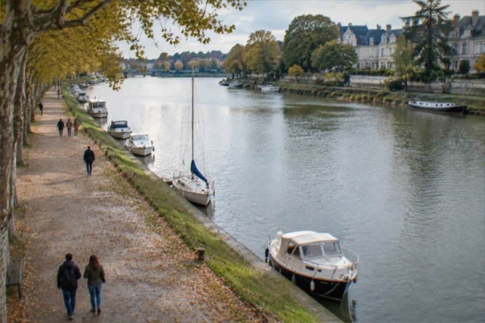 Visitors on a wide tree-lined path by the Erdre river in Nantes in warm autumn light