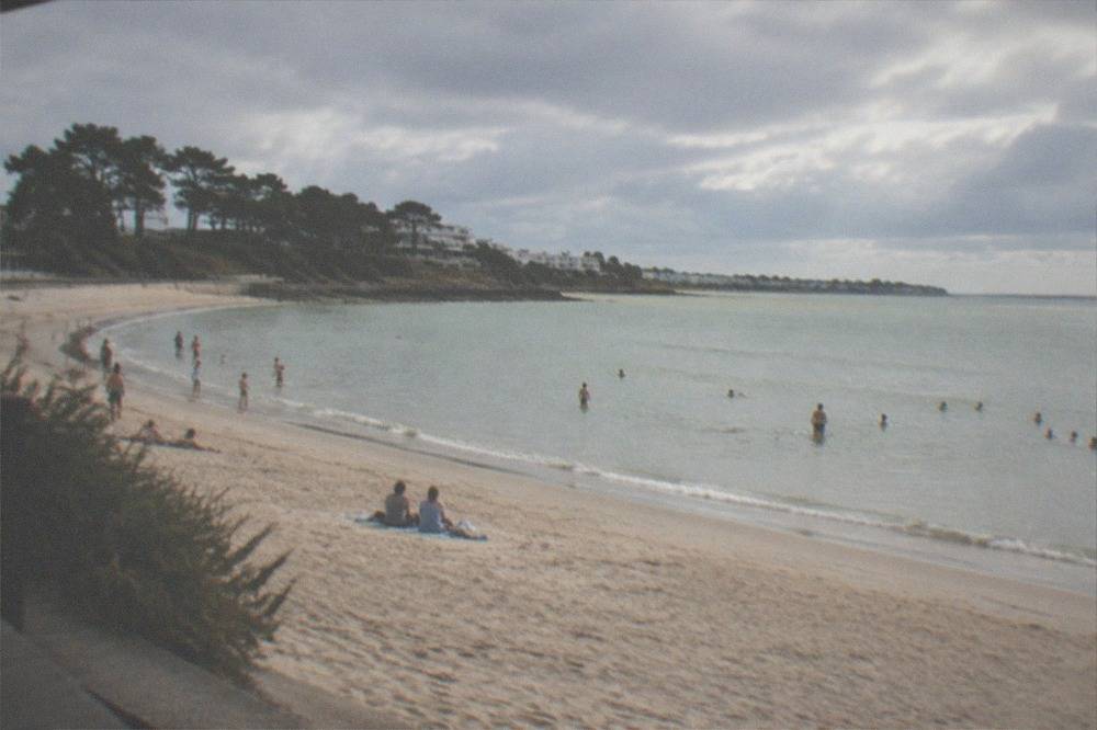 People swimming in calm sea near a sandy cove on a bright summer afternoon