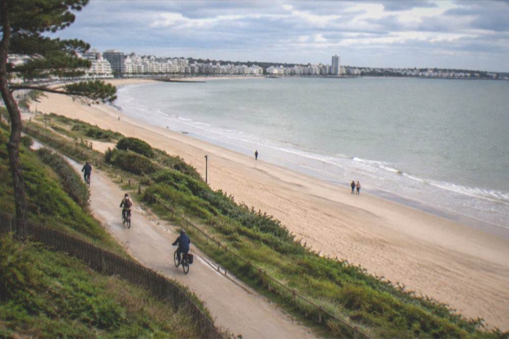 Cyclists riding along a riverside path with the city skyline behind them
