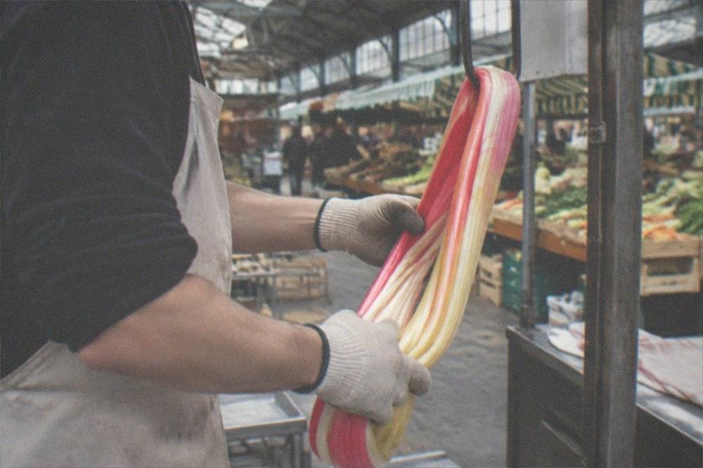A confectioner pulling and folding a rope of coloured sugar on a hook in a workshop