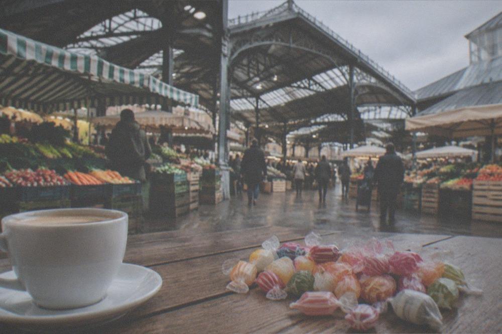 A mixed bag of berlingot candies in different colours spread on a wooden table beside a cup of coffee