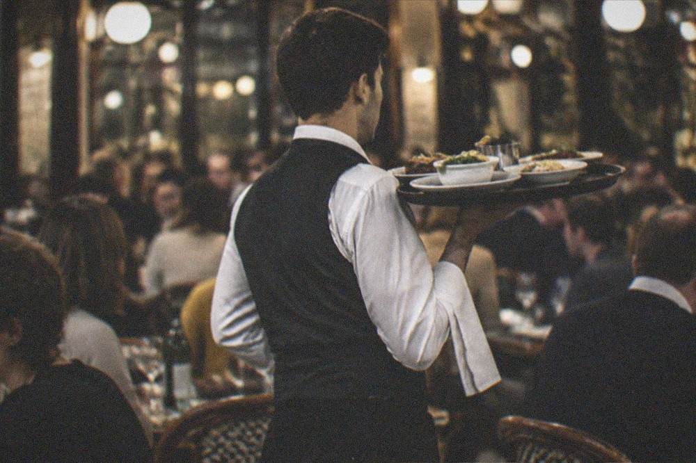Waiter carrying a tray of dishes through a busy French brasserie at night