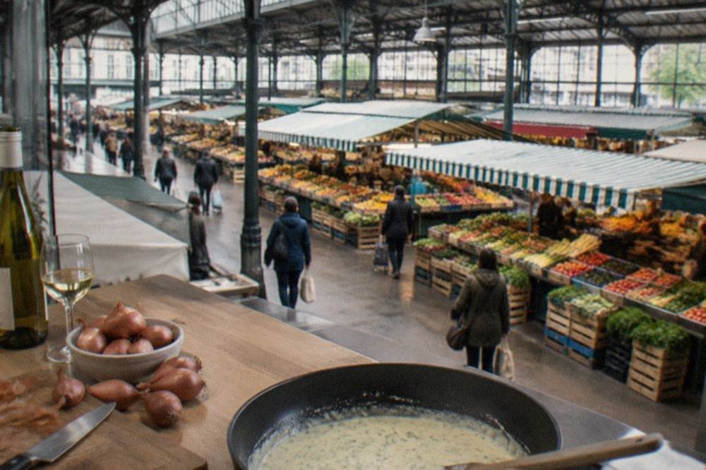 Shallots and a bottle of white wine next to a pan of pale sauce on a kitchen counter