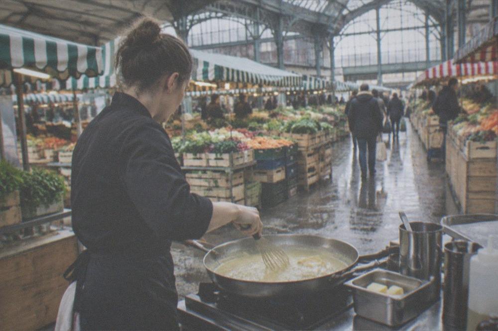 A cook whisking butter into a shallow pan of pale sauce over a stove