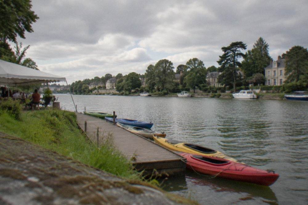An open-sided tent in summer beside the Erdre river, kayaks tied up at a small wooden pontoon