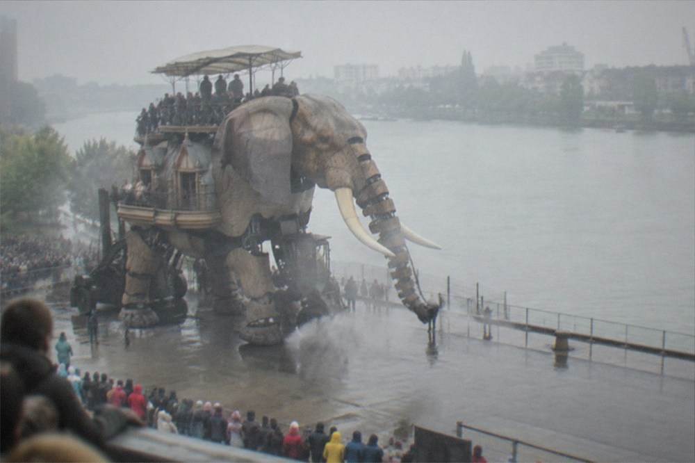 Visitors watching the mechanical elephant walk along the quay on the Île de Nantes, steam rising and crowd behind barriers