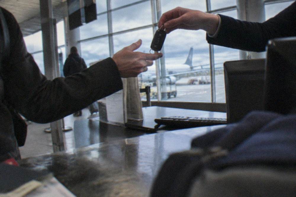 A rental agent handing car keys to a traveller over an airport counter