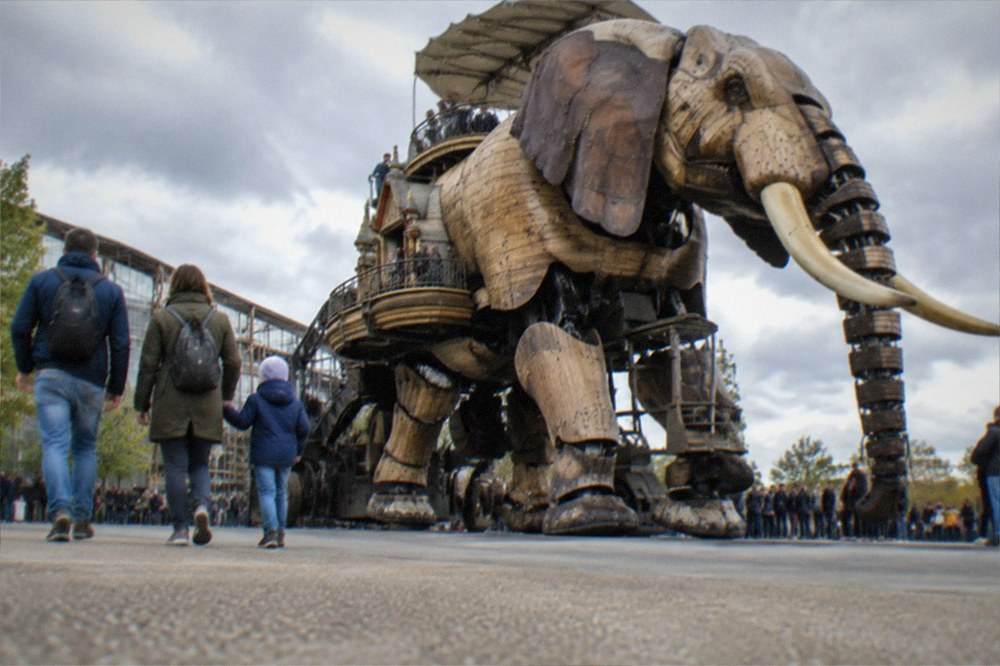 A family walking beside the mechanical elephant at Les Machines de l'ile in Nantes