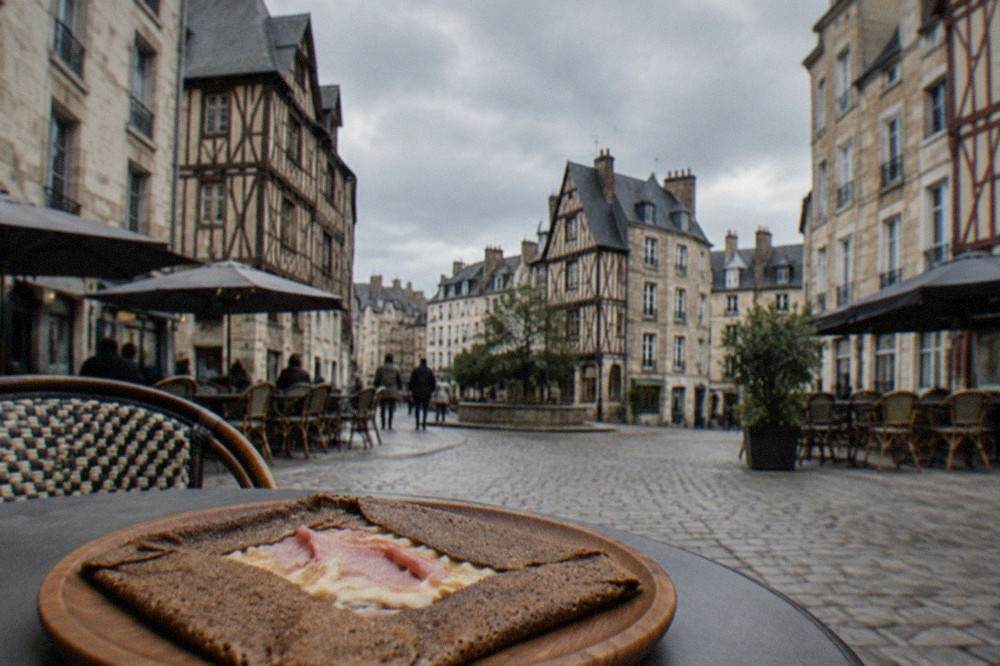 A buckwheat galette filled with ham and melted cheese folded on a wooden plate