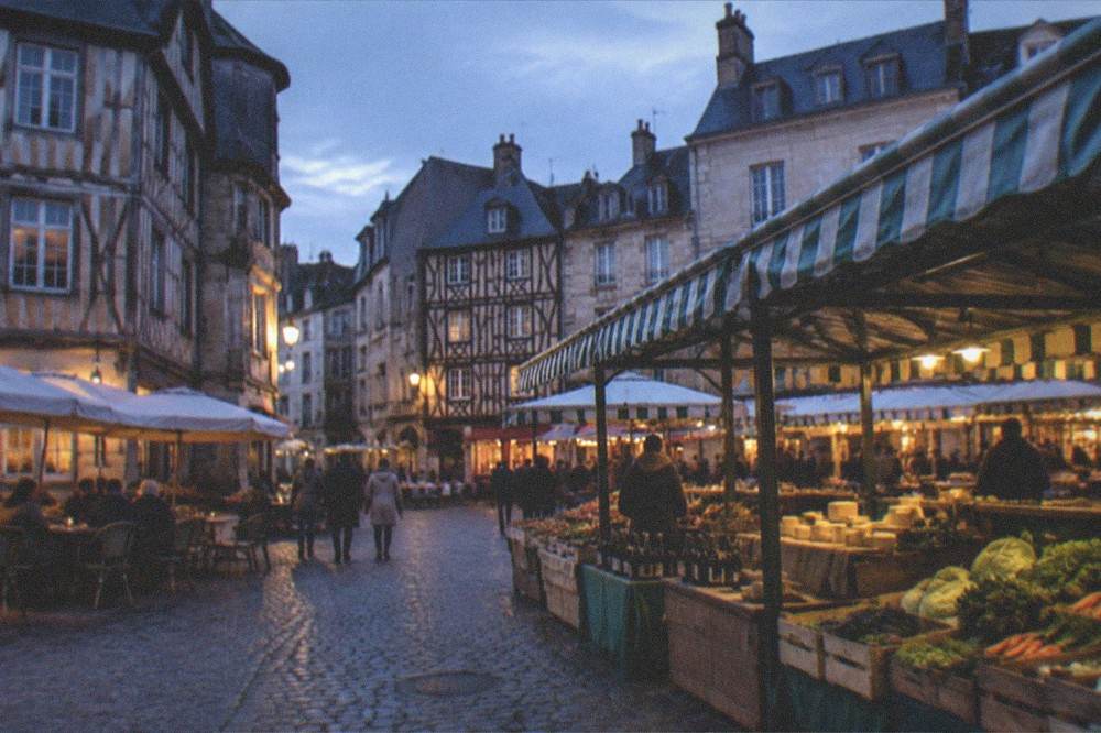 A covered market hall with stalls of vegetables, cheese and cider bottles under striped awnings