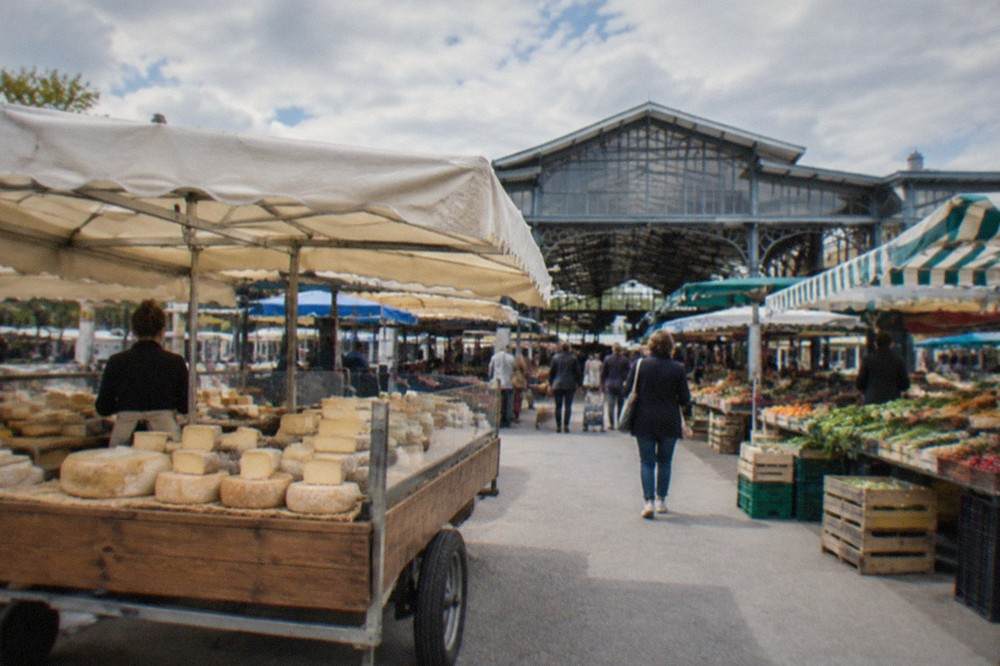 A cheesemonger's stall with wheels and squares of cheese under the awning of a French market