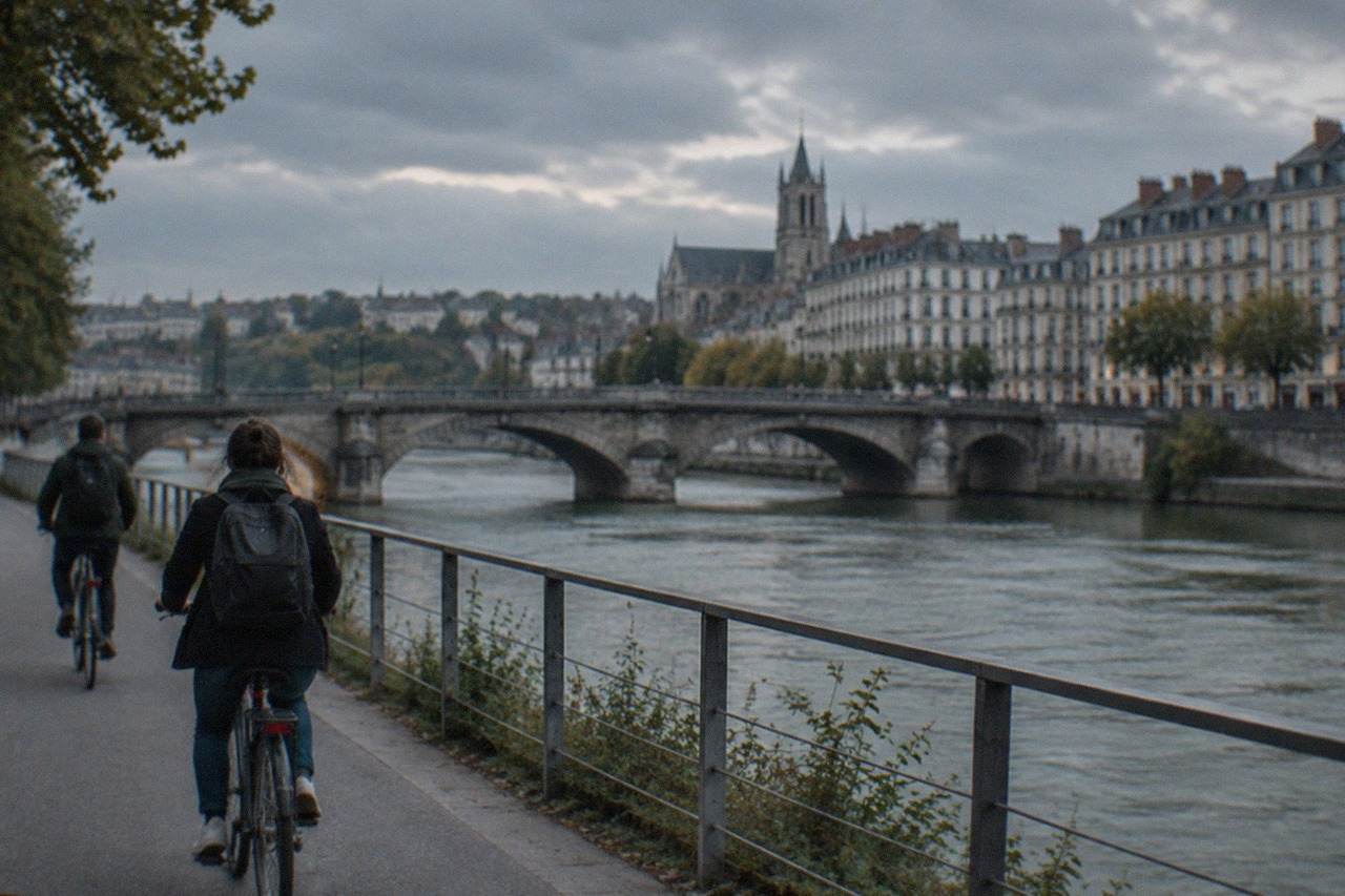 Cyclists riding along a riverside path in Nantes with a stone bridge over the water behind them