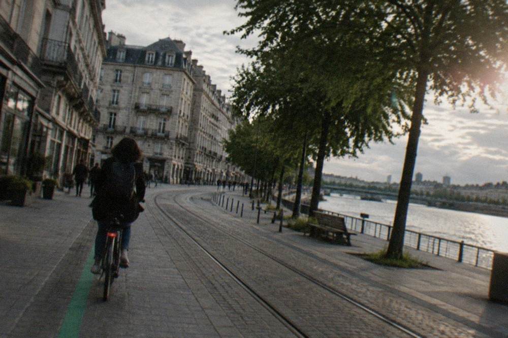 A cyclist following a green painted line along a Nantes street lined with shops