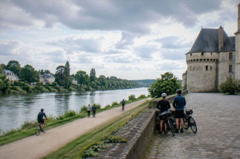 Cyclists resting beside a castle wall with a wide stone courtyard beyond