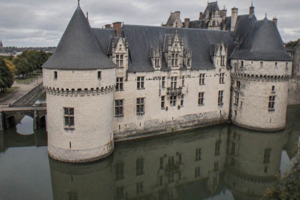 A close view of the white tufa and dark slate of the château's grand facade with its balanced towers reflected in the moat below