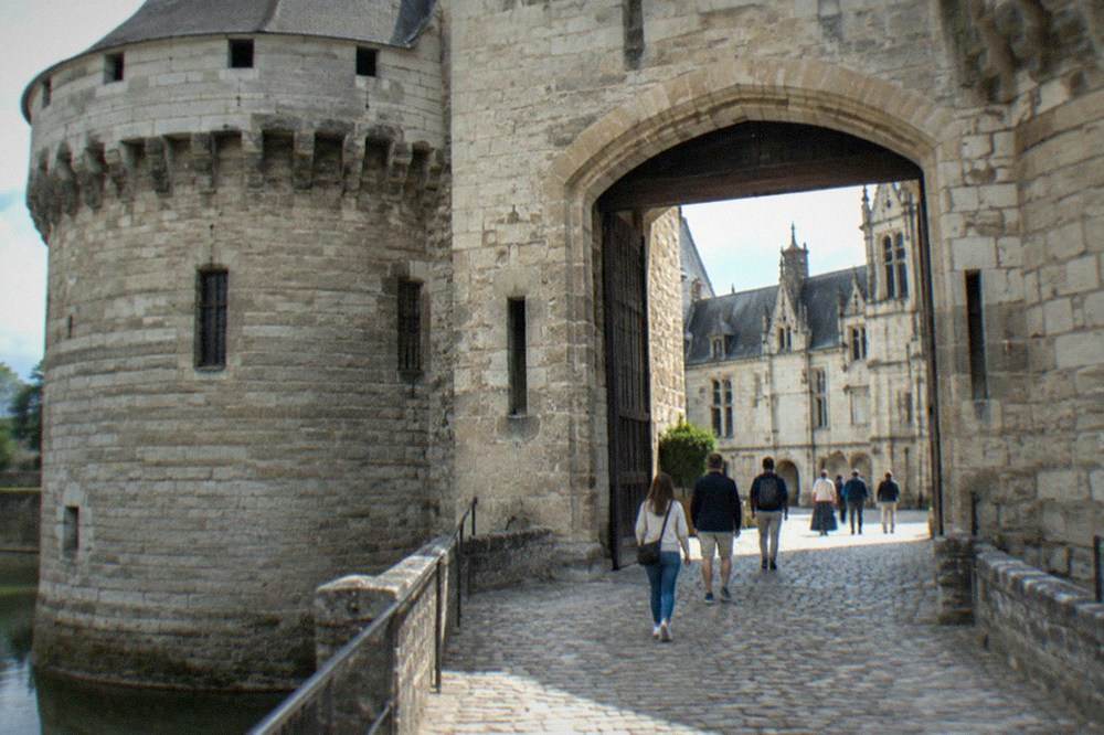 Visitors walking through the archway entrance of the château into the cobbled interior courtyard on a sunny afternoon