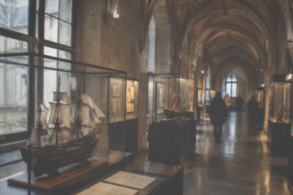 A museum gallery inside the château with model ships, archive documents and display cases lit softly along the stone vaulted corridor