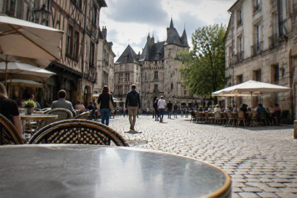 Sunlit tables and pedestrians on a cobbled street in the Bouffay quarter near the château with cafe awnings and old stone facades