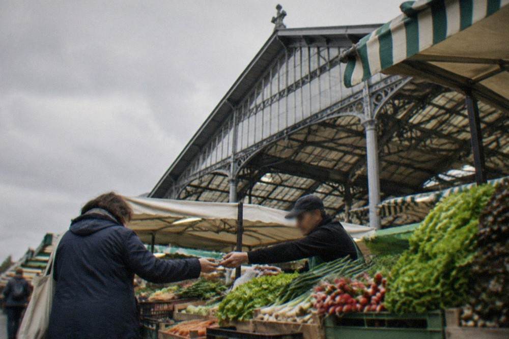 A market stallholder at Talensac market handing change to a customer over crates of vegetables