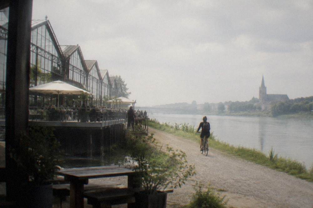 A cyclist on a gravel towpath beside the wide Loire with a village church in the distance