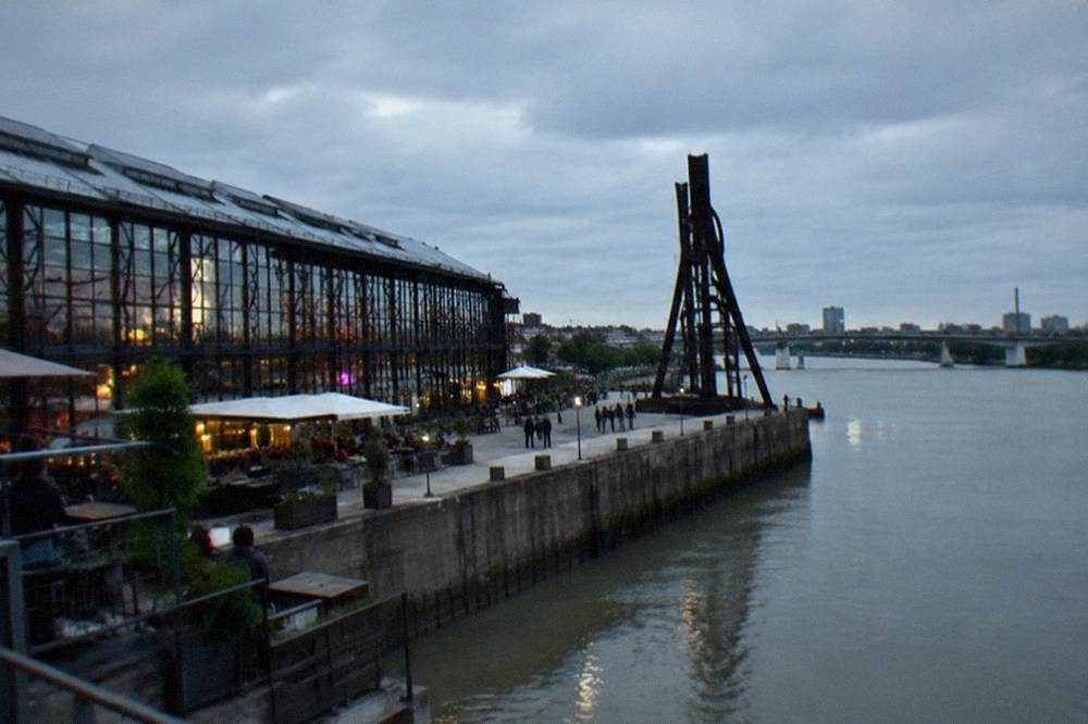 A large steel sculpture standing on a concrete quay against a grey sky
