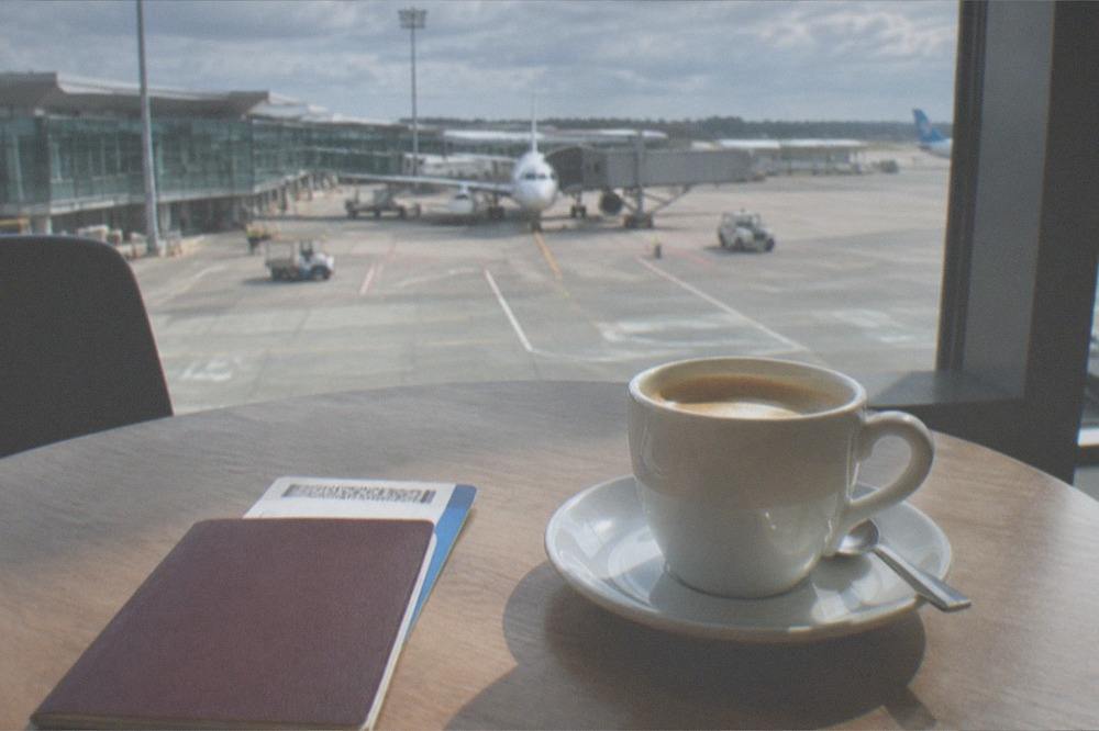 A passport and boarding pass resting on a cafe table beside a coffee cup before a flight