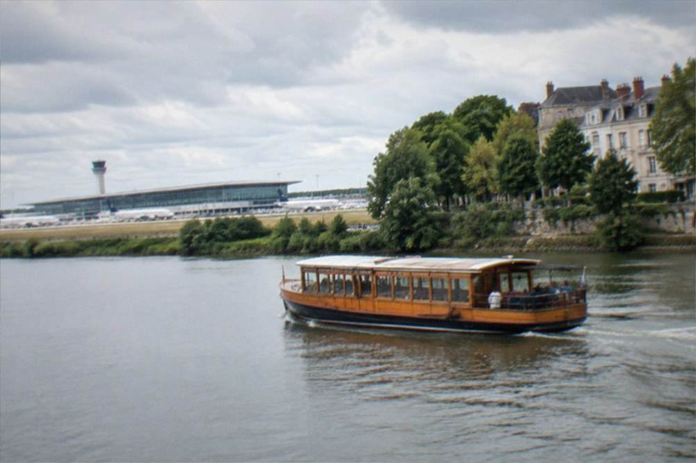 A wooden sightseeing boat cruising along a tree-lined river with grand houses on the bank
