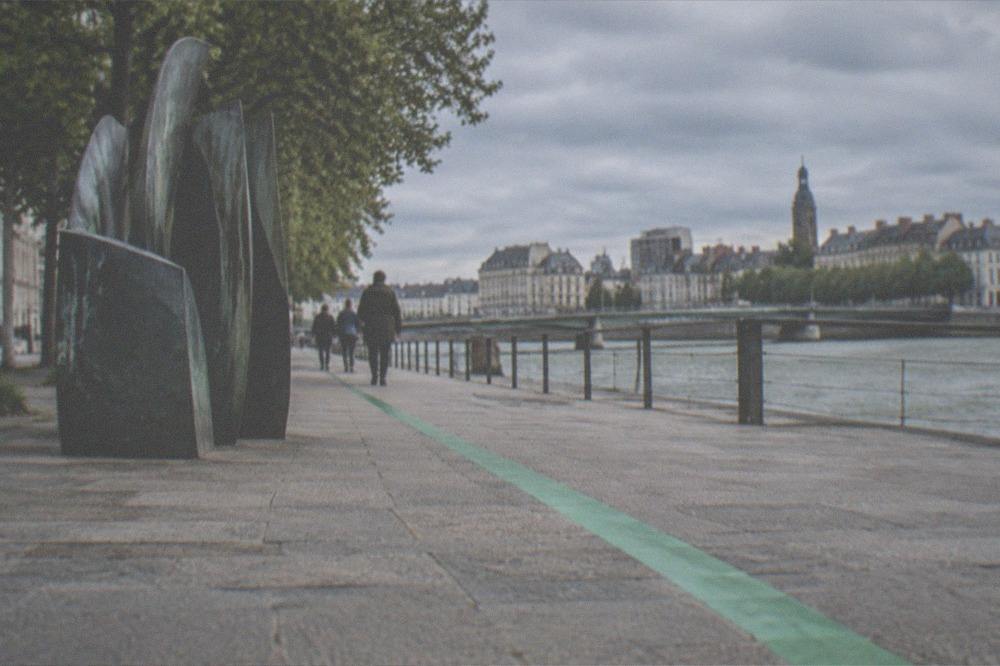 A green painted line running along a Nantes pavement past a contemporary public artwork