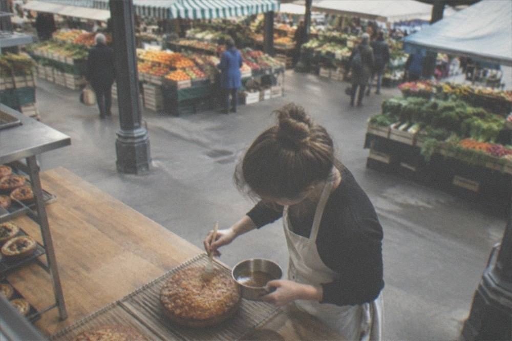 A baker brushing rum syrup over the top of a freshly baked almond cake on a wire rack