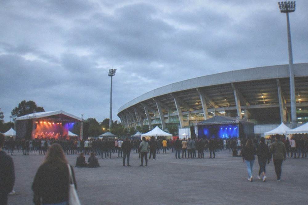 Two small festival stages with tents and crowds spaced across open festival grounds in daylight