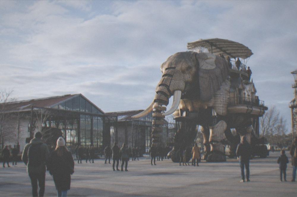 People strolling past a large mechanical elephant sculpture on an island promenade in Nantes