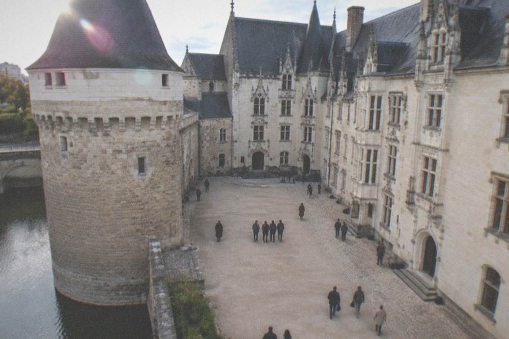 Visitors strolling the courtyard of the Chateau des ducs de Bretagne beside the pale stone palace facades