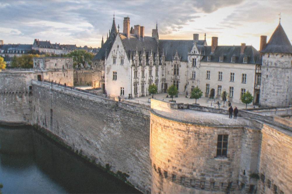 Evening light on the ramparts of the Chateau des ducs de Bretagne with walkers along the stone walls