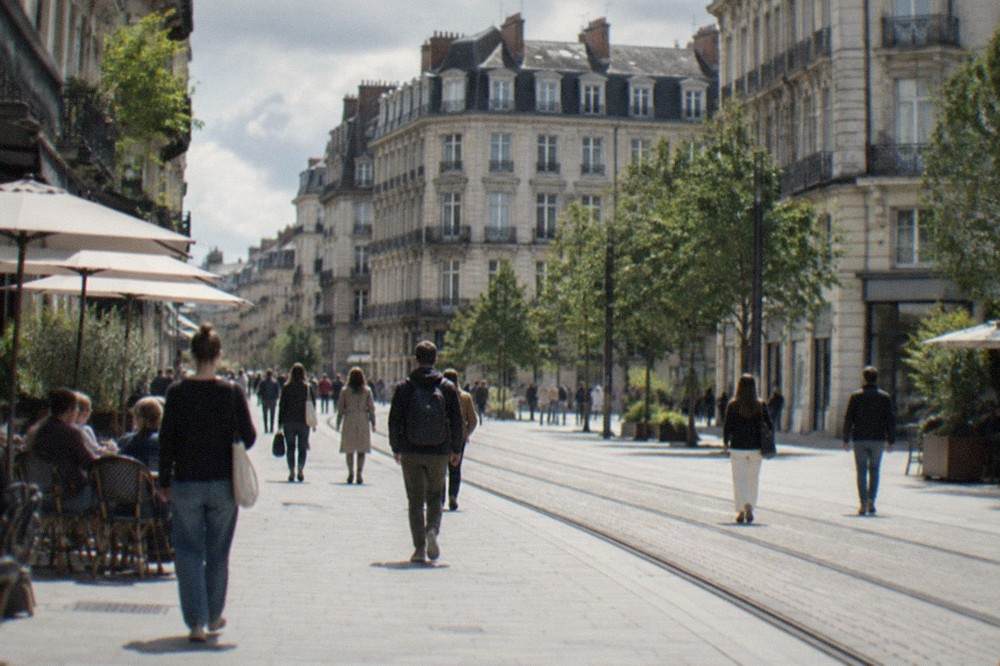 People walking along a sunlit pedestrian shopping street in central Nantes with café tables along the pavement
