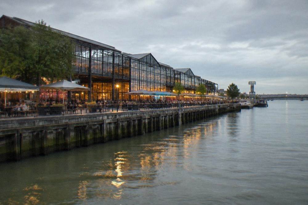 Evening view of the illuminated Hangar à Bananes riverside strip on the Île de Nantes with people outside bars