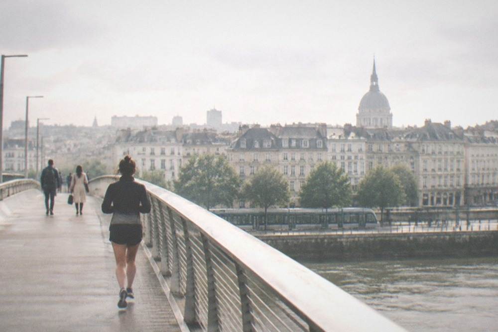Travellers crossing a modern bridge over the Loire with the Nantes skyline and a tram passing below