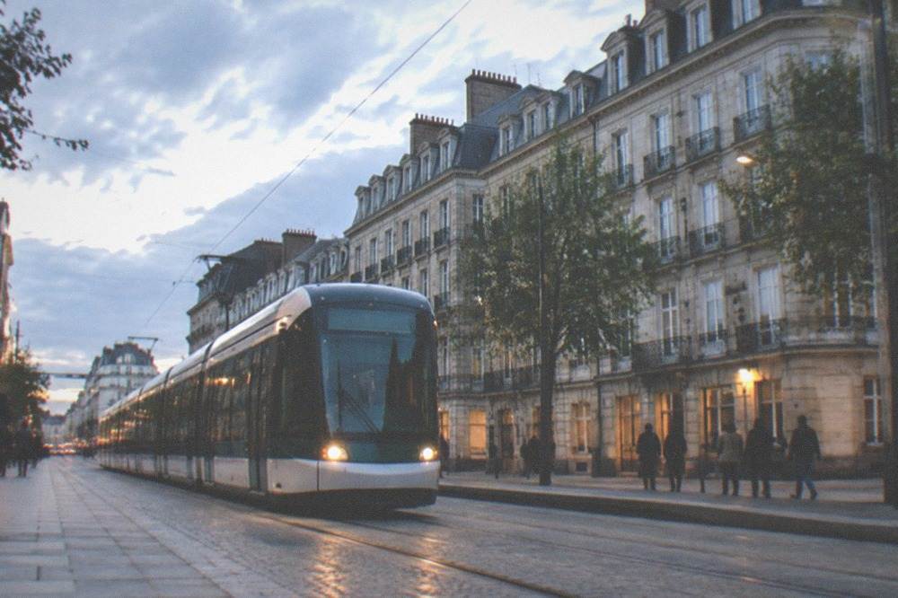 Modern Nantes tram in its own lane on a city street lined with stone buildings and pedestrians