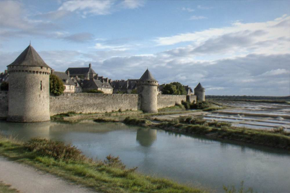 Walled medieval town of Guérande seen from outside its ramparts with stone towers and rooftops under a blue sky