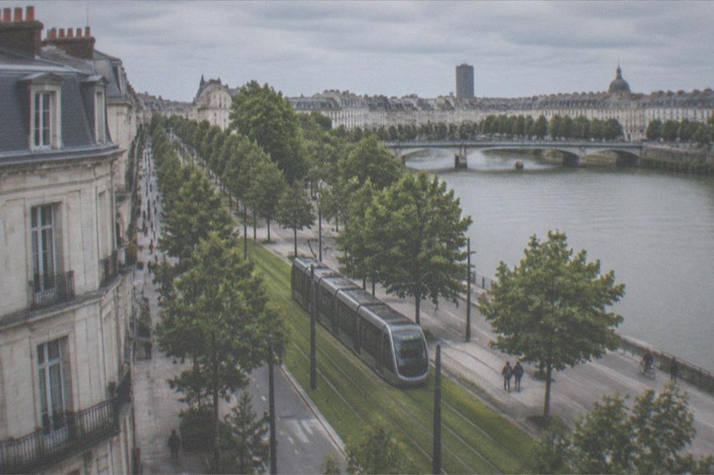 A modern tram moving along a grass-lined track through a Nantes street