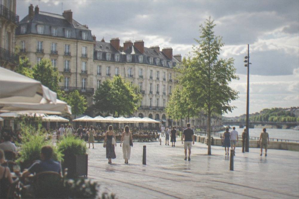 People strolling along a sunlit Nantes square lined with cafes in summer