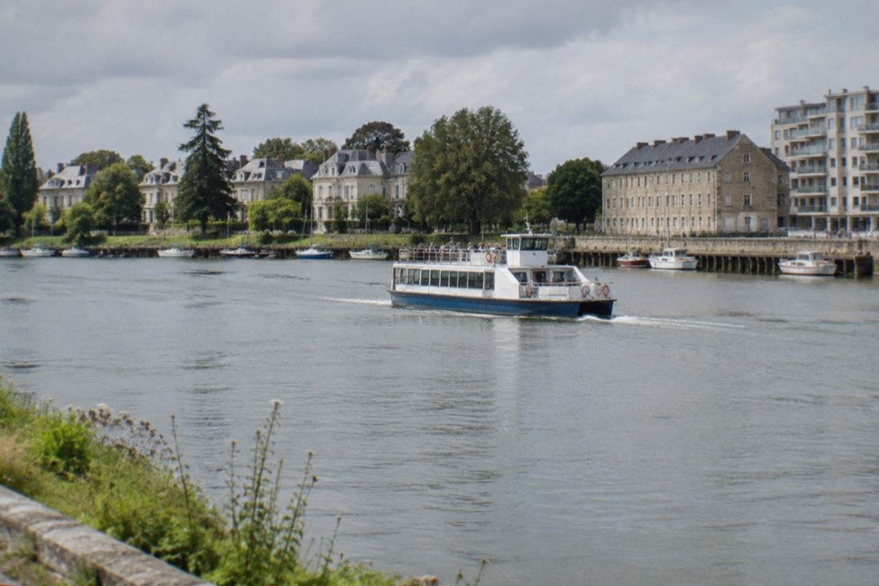A passenger ferry crossing a wide French river towards a quayside of stone warehouses and modern apartment blocks