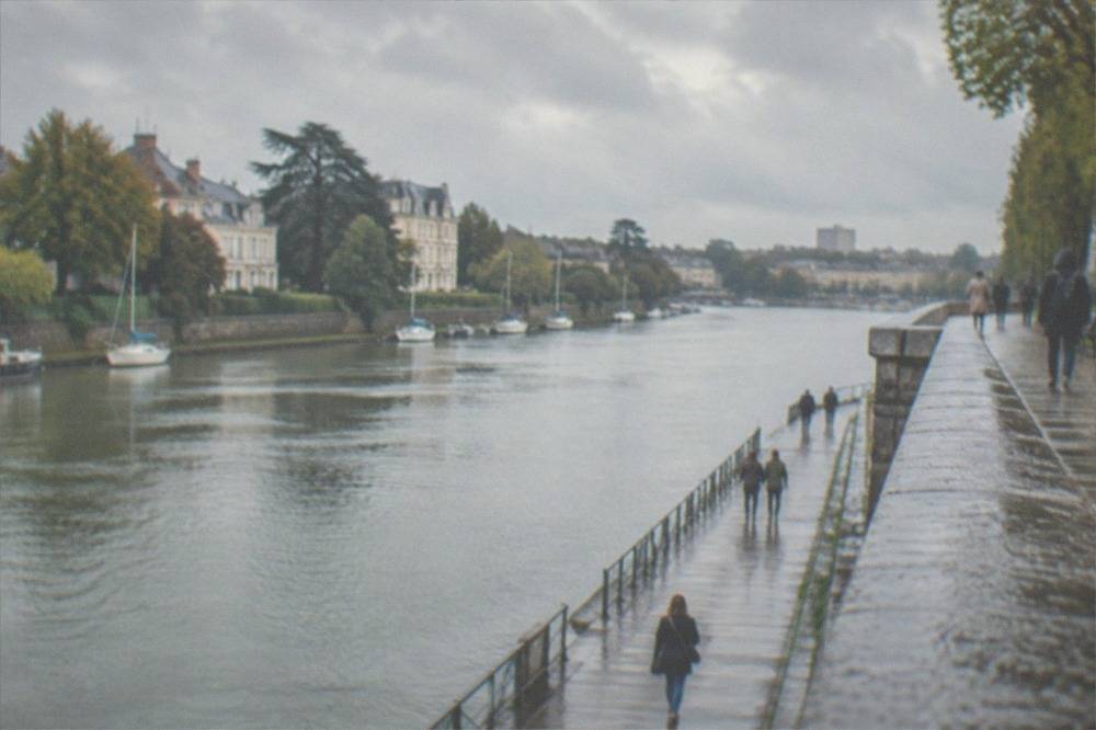 A long grey stone quay beside a wide river with a memorial walkway set into the lower wall and people strolling along it