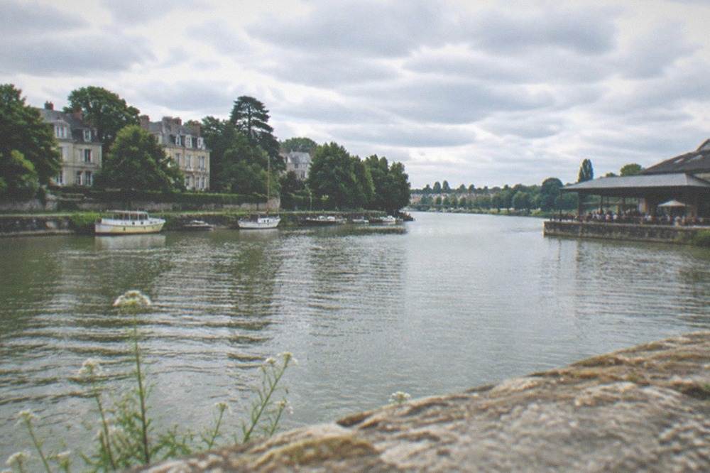 A warehouse building with a wide covered terrace on a riverside quay, with tables and people along the water