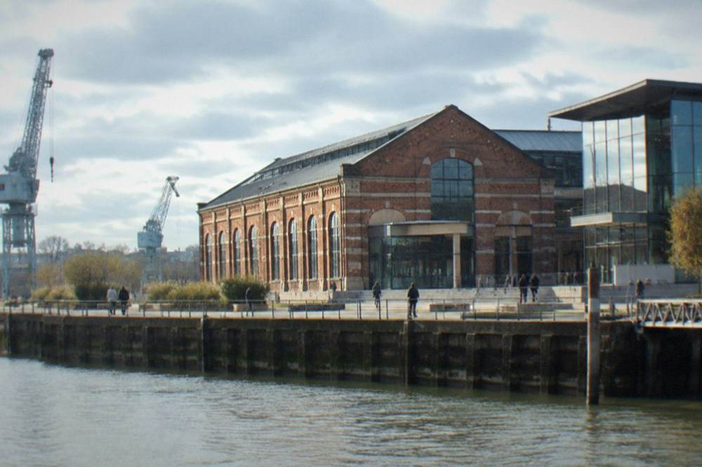 A nineteenth-century industrial brick building beside a river quay with a modern cultural centre entrance