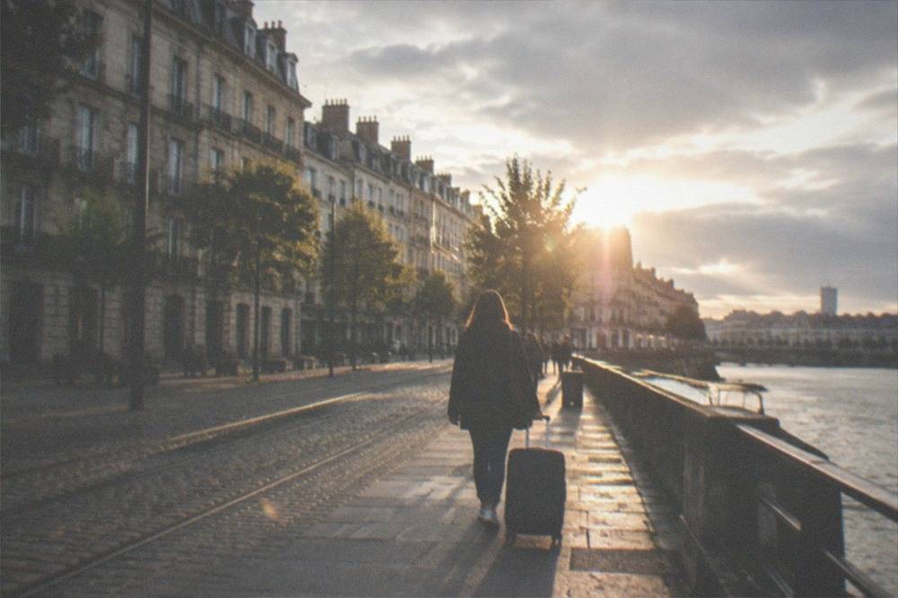 A traveller with a suitcase walking along a sunlit street in central Nantes